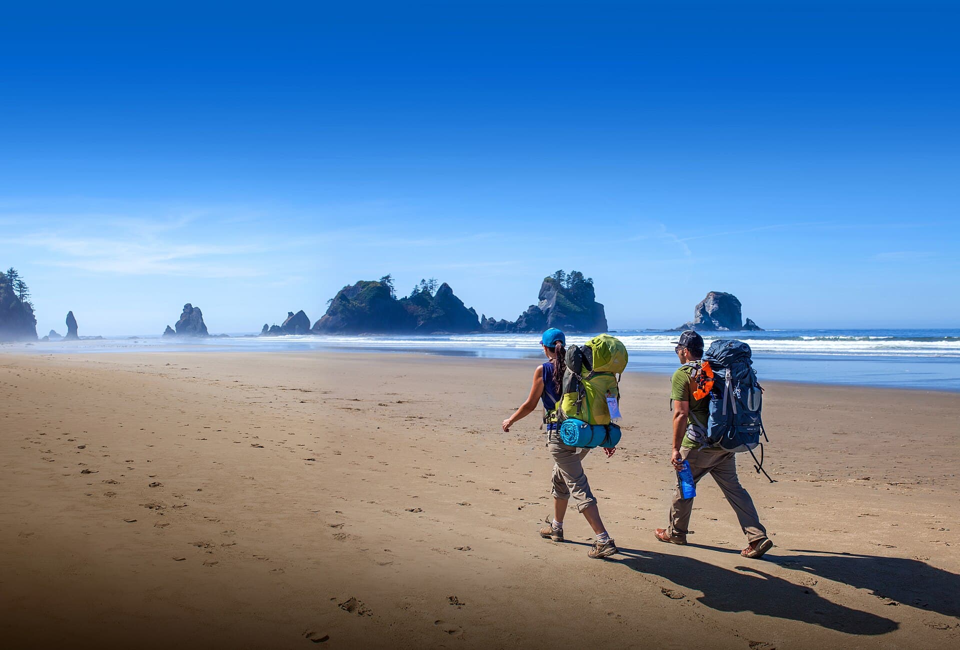 Dos mochileros caminando por una playa con rocas en el mar
